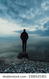 Silhouette of man standing alone on a rock in the water at dusk.