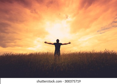 silhouette of man standing in a field at sunset