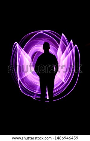 Silhouette of a man standing from the front. Curved abstract shapes made of violet light saber in background. Lightpainting session in long exposure at night.