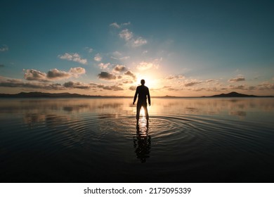 Silhouette of a man standing with his back facing at sunset over the shallow waters of the Mar Menor, Region of Murcia, Spain, creating ripples on the surface of the water