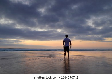 Silhouette of a man standing on the beach on a cloudy morning watching the sunrise.