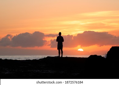 Silhouette of a man standing on a rocky coastline line at sunrise.