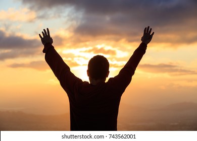 Silhouette of man standing with open hands looking at the golden sun. Peaceful view. - Powered by Shutterstock