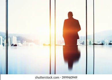 Silhouette of a man successful lawyer is thinking about the future of an important court session, while is standing in modern office interior near big window with view of developed New York city
