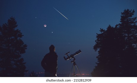 Silhouette of a man, telescope, stars, planets and shooting star under the night sky. - Shutterstock ID 2152812939