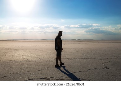 Silhouette Of Man Walking Alone On Dried Lake. Young Man Walking Alone In The Desert