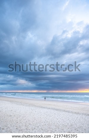 Silhouette of a man walking along the beach on a cloudy day.