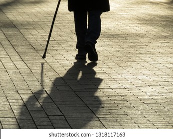 Silhouette Of Man Walking With A Cane, Long Shadow On Pavement. Concept Of Blind Person, Limping, Disability, Old Age, Diseases Of The Spine