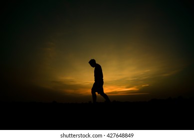 Silhouette of a man walking with a sad look on after sunset.