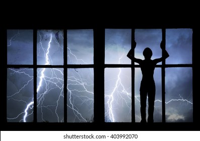 Silhouette Of Man Watching Lightning, Thunder, Rain And Storm Through Broken Window Of Old Building.