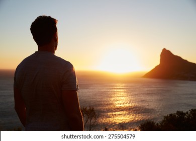 Silhouette Of Man Watching Sun Set Over Sea And Cliffs