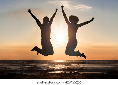 Silhouette Of Man And Woman Jumping At Beach During Sunset