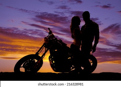 A silhouette of a man and woman next to a motorcycle in the outdoors.