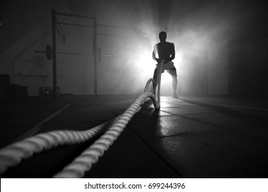 Silhouette of man working out with battle ropes at gym. Functional training. Sports and fitness concept.