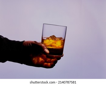 Silhouette of mans hand holding a glass of whisky. 