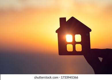 silhouette of man's hand holding small wooden house against sunset or sunrise light, sweet home and family concept, real estate agent offer new house for rent, copy space  - Powered by Shutterstock