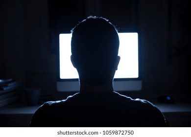 Silhouette of man's head in front of computer monitor light at night - Shutterstock ID 1059872750