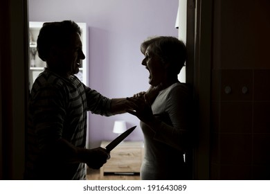 Silhouette of mature couple fighting, the man is attacking woman with knife. Woman is victim of domestic violence