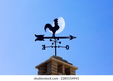 Silhouette of a metal frame weathercock on the roof with the moon in background.