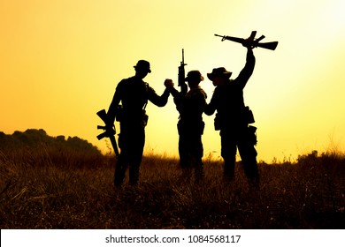 Silhouette Of Military Soldier Holding Weapons Overhead After Get Victory Of War At Sunset.