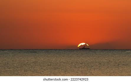 Silhouette Of A Military Vessel Ship On The Sea Shore Against Sunrise Orange Sky. Military Industry Landscape.