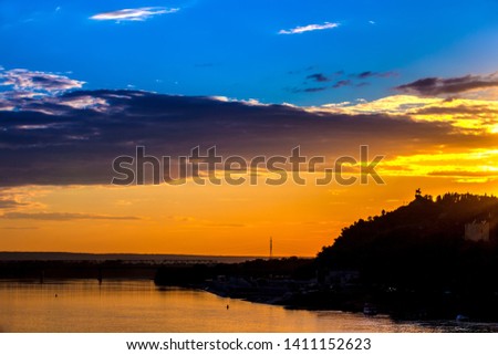 Silhouette of monument to Salawat Yulaev against a bright yellow blue sky with clouds and orange sun disk at city sunset on the river bank. Salavat Yulayev, Ufa, Bashkortostan, Russia.