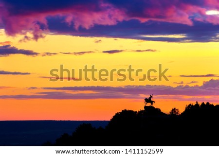 Silhouette of monument to Salawat Yulaev, folk hero on a horse against a bright yellow purple violet sky with clouds and orange sun disk at city sunset. Salavat Yulayev, Ufa, Bashkortostan, Russia.