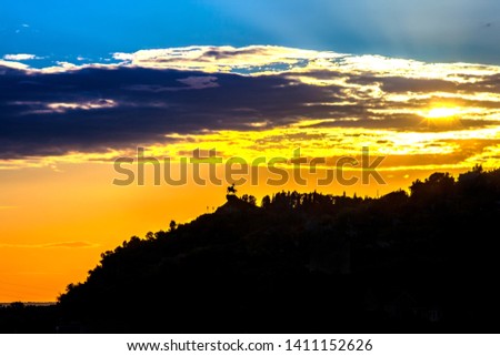 Silhouette of monument to Salawat Yulaev, folk hero on a horse against a bright yellow blue sky with clouds and orange sun disk at city sunset. Salavat Yulayev, Ufa, Bashkortostan, Russia.