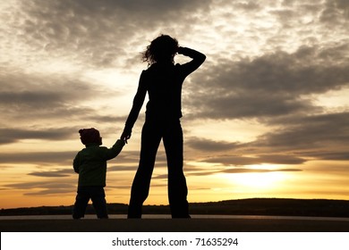 Silhouette of mother and baby looking away into the sunset and water
