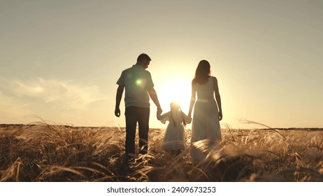 Silhouette of mother with father holding hands of funny daughter jumping over grass. Wife and husband walk looking at daughter strolling and jumping. Mother with father walking at sunset on field - Powered by Shutterstock