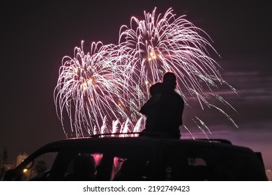 silhouette of a mother with her little daughter watching fireworks on the roof of their car