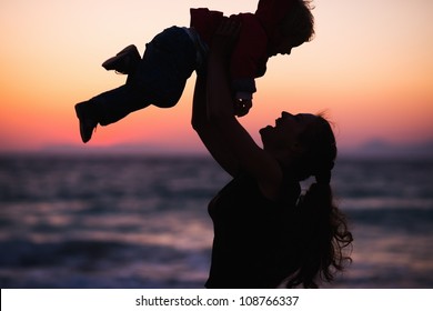 Silhouette Of Mother Throwing Baby Up On Sunset