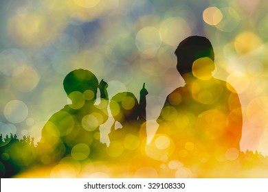 Silhouette Of Mother And Two Kids. Little Children Point To Sky. Twinkling Lights Vivid Blurred Bokeh Abstract In Yellow Background. Friendly Family.