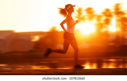 Silhouette With Motion Blur Of A Woman Athlete Running At Sunset Or Sunrise. Fitness Training Of Marathon Runner.