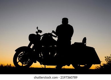 Silhouette Of Motorcycle And Motorcyclist Biker In Early Morning Or Late Evening Alone Looking At Sunrise Or Sunset During Cross Country Road Trip