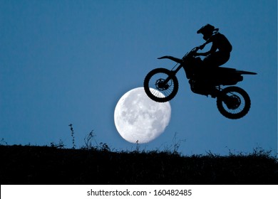 Silhouette Of A Motorcycle Racer Commits High Jump On Night Sky With The Moon