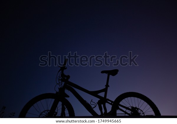 Silhouette of Mountain Bike, Dirt bike on the car\
roof rack in the countryside at the sunset,Bicycles built for\
traveling on dirt\
road.