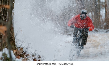 Silhouette of a mtb rider appearing through spraying snow cloud at forest trail. Extreme bike riding in the woods after fresh snowfall. Mountain biking in winter conditions on snow-covered trails. - Powered by Shutterstock