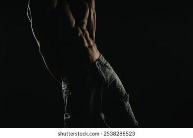 Silhouette of a muscular man's torso showing defined abs and wearing jeans, captured in dim lighting. - Powered by Shutterstock