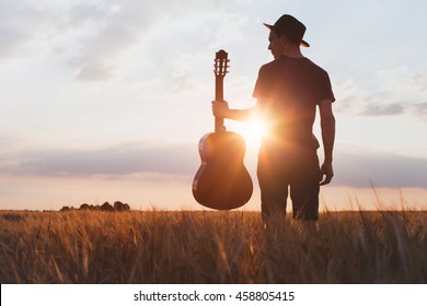 silhouette of musician with guitar at sunset field, music background