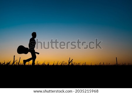 Silhouette of a musician holding a guitar and walking along the horizon at sunset