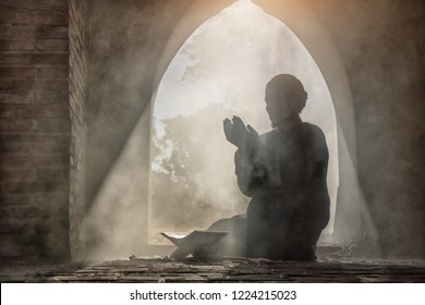 Silhouette of muslim man having worship and praying for fasting and Eid of Islam culture in old mosque with lighting and smoke background