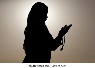 Silhouette of muslim woman holding prayer beads in   her hands and praying against the sky. Religion praying concept. United Arab Emirates