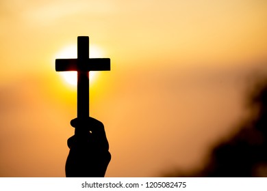 Silhouette off woman hands holding wooden cross on sunrise background, Crucifix, Symbol of Faith.