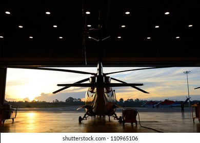 silhouette of offshore oil rig  helicopter in the hangar next to runway with sunrise background .