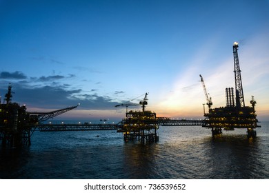 Silhouette Of Offshore Production Platforms Connected With Bridge During Sunset At Oilfield