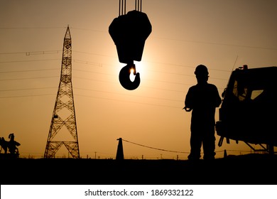Silhouette of oilfield worker in the oilfield with crane hook  at sunset