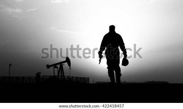 Silhouette of oilfield worker\
and crude oil pump in background- oilfield  - sunset - Black and\
white