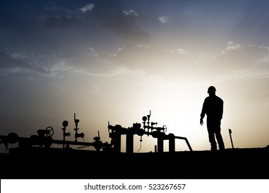 Silhouette of oilfield worker monitoring manifold valves in oilfield at sunset