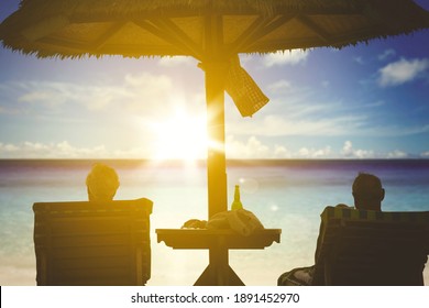 Silhouette of old couple relaxing on the sunbed while enjoying sunset view. Shot in the tropical beach - Powered by Shutterstock